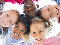 Young children grouped up with arms around each other looking down at the camera