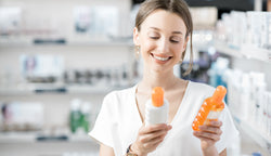 A young woman choosing between multiple types of sunscreen.