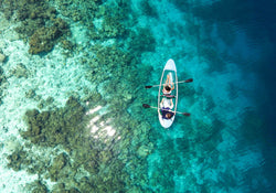 People kayaking across a reef with the suns reflection next to them.