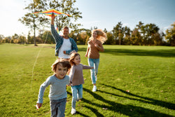 Children running with parents across a grassy field in the sun.